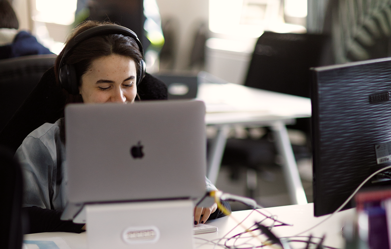 Person wearing headphones working on a laptop at a desk in an office setting.