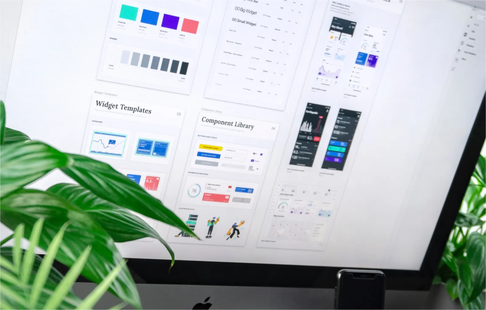 Computer screen displaying design templates and component library for widgets, partially obscured by green plant leaves and an iPhone at the bottom.